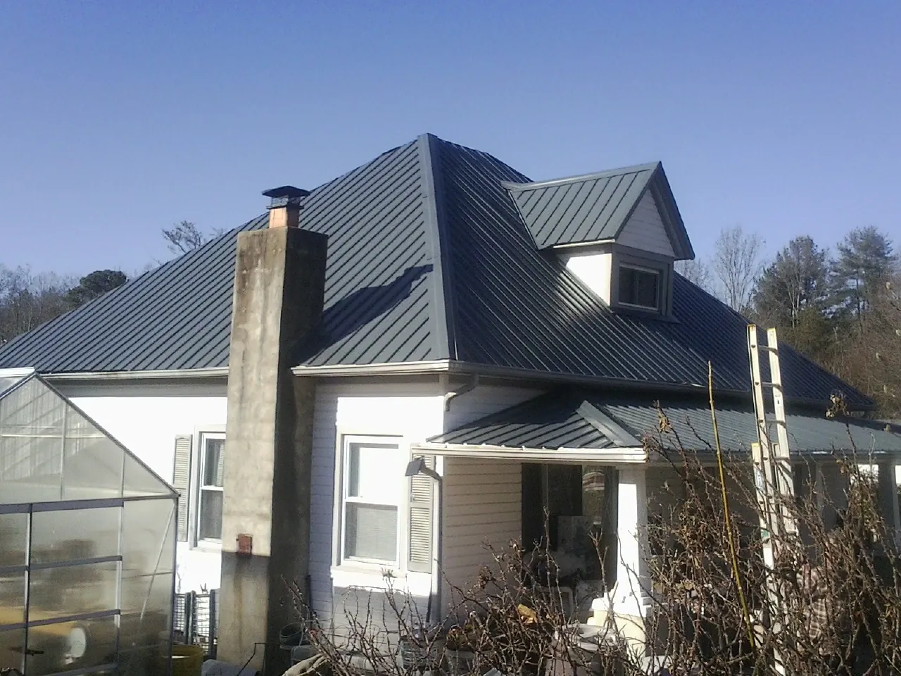 Dark blue standing seam metal roof on a white farmhouse with dormer — Slate & Tile Roof Repair by Roofing Brothers in Nakina