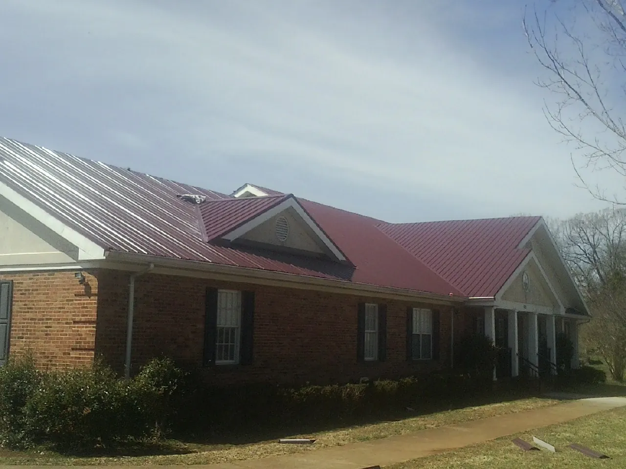 Red metal roof with gabled entries on a long brick building, from a Hail Damage Roof Repair job in Nakina