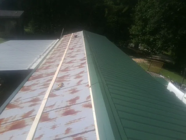 Old rusted panels beside newly installed green metal roofing in Nakina