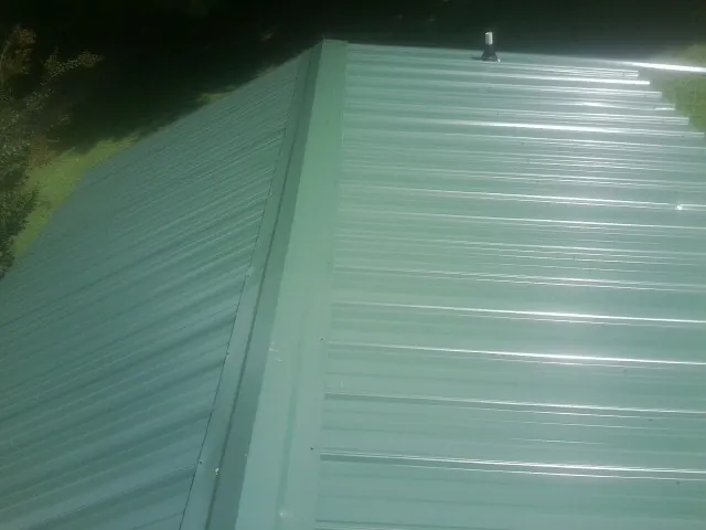 New green metal panels meeting at the ridge of a roof — Flat Roof Repair work by our crew in Nakina
