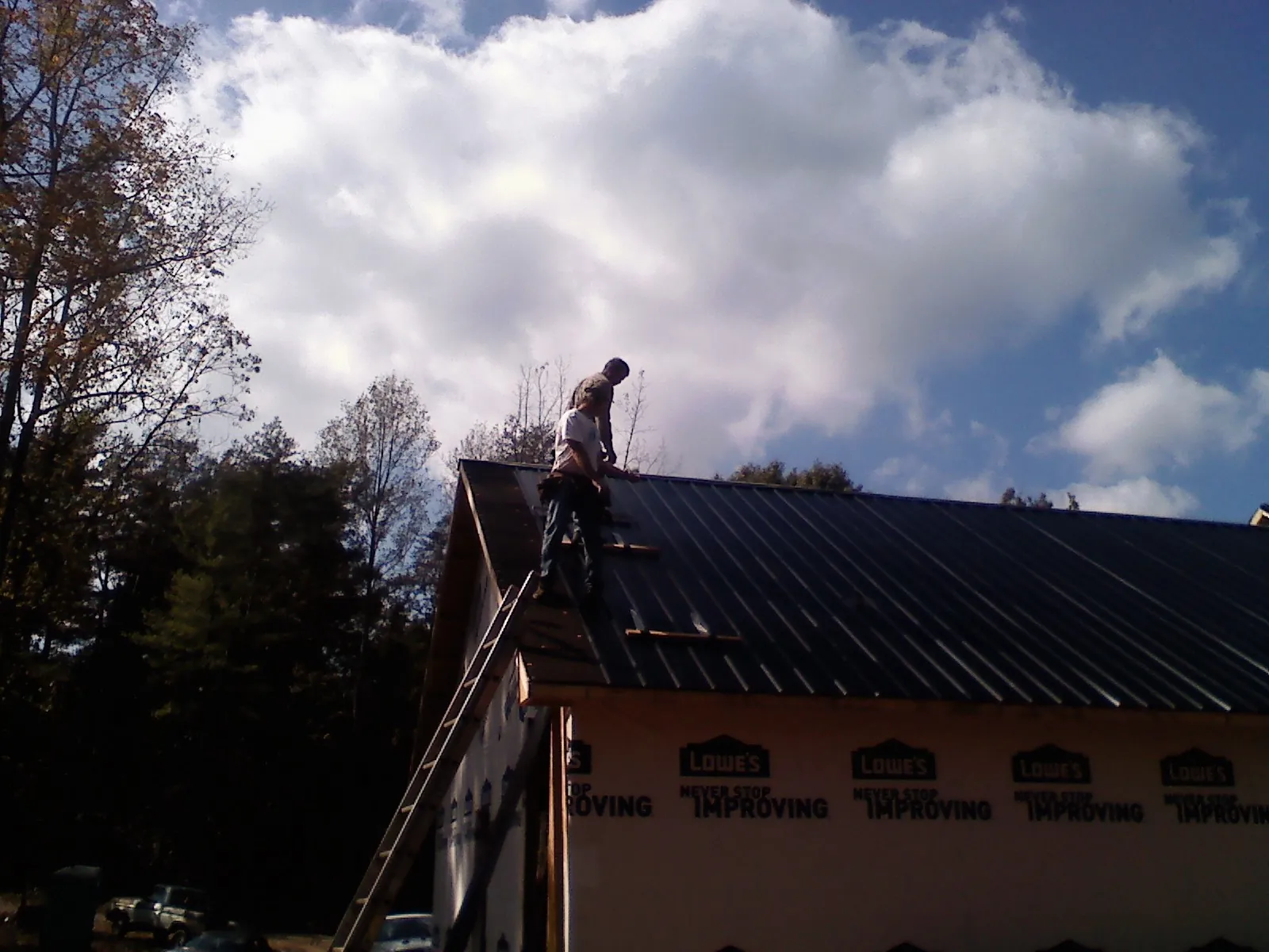 Roofer fastening dark metal panels high against a cloudy sky, from a Roof Inspection job in Nakina