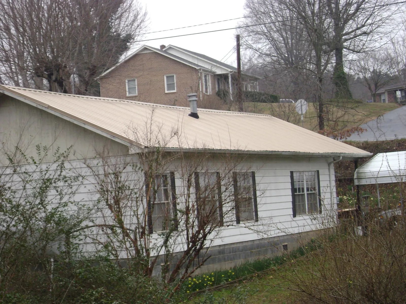 Tan metal roof on a white sided house set into a hillside — Commercial Roofing by Roofing Brothers in Nakina