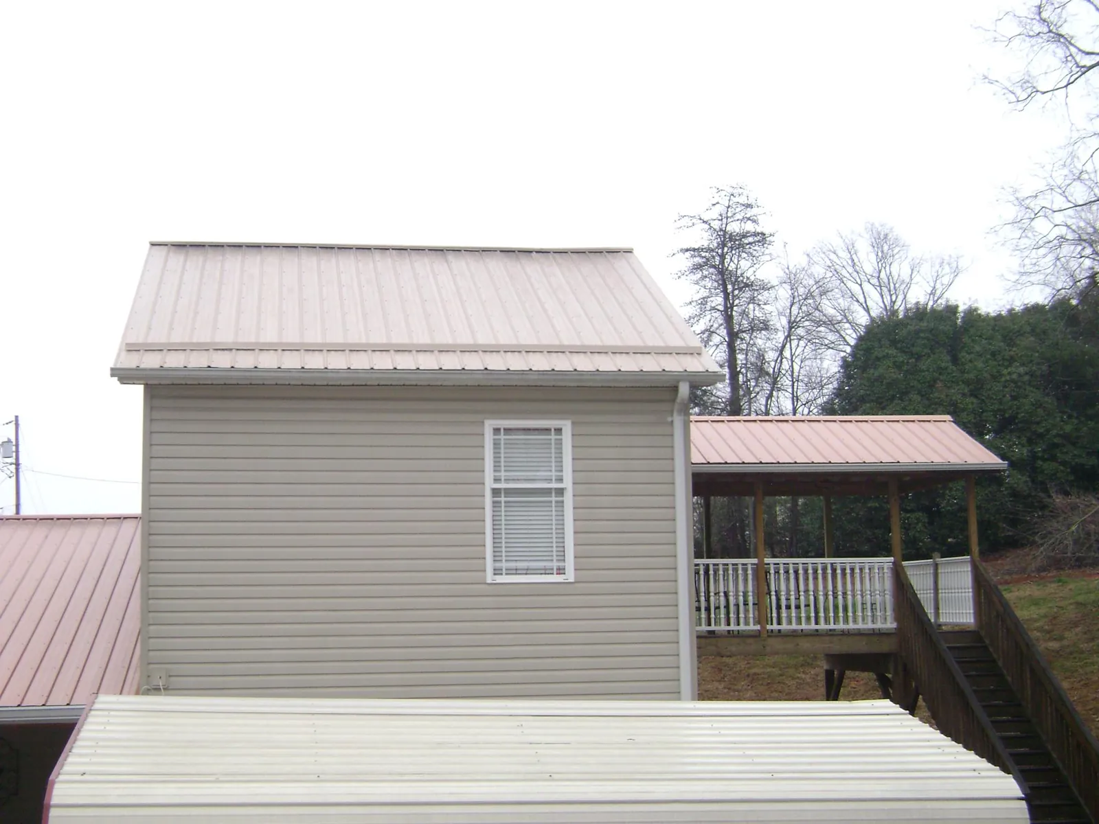 Tan metal roofs on a two story addition and attached porch, from a Roof Replacement job in Nakina